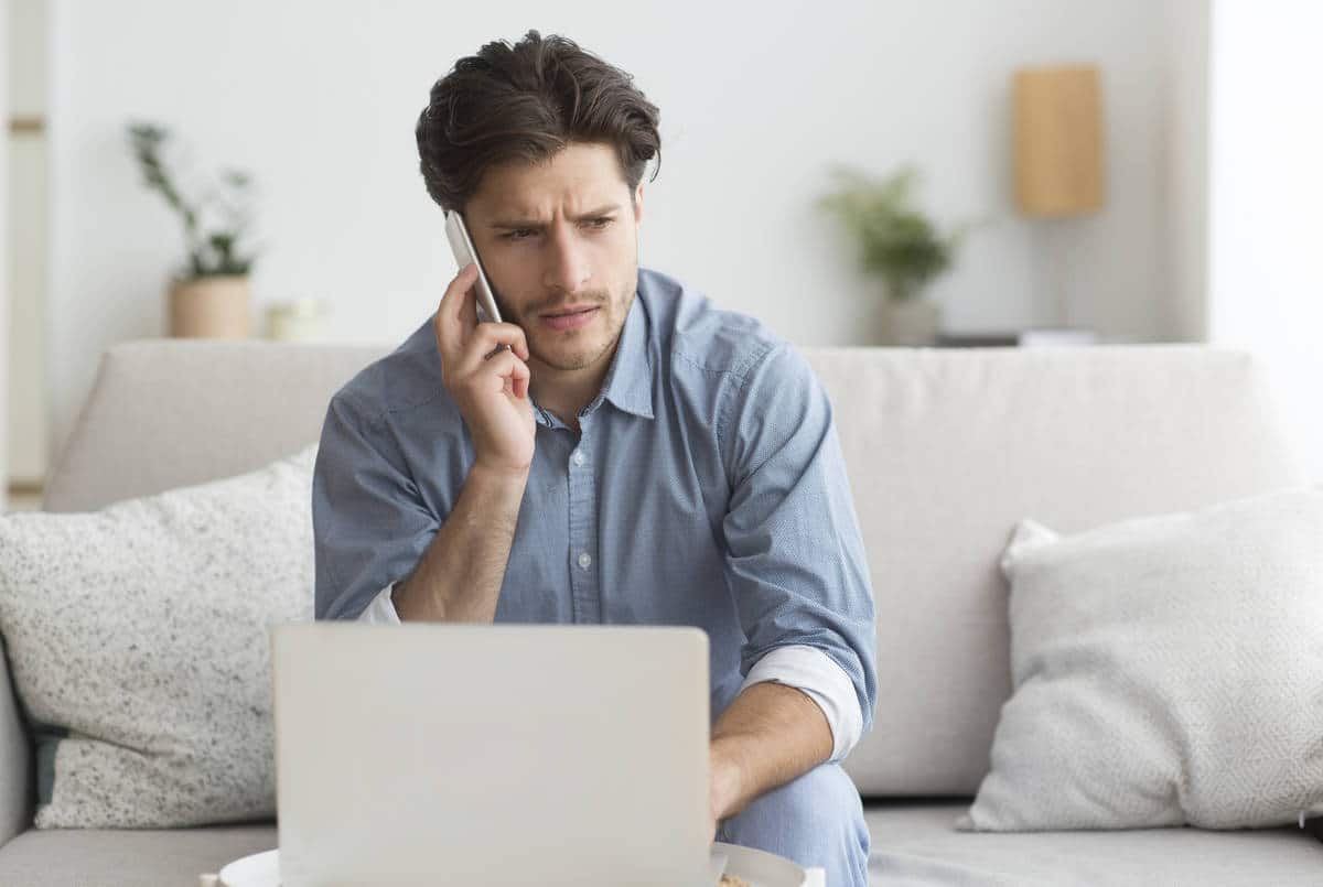 Guy Having Unpleasant Phone Conversation Working On Laptop At Home