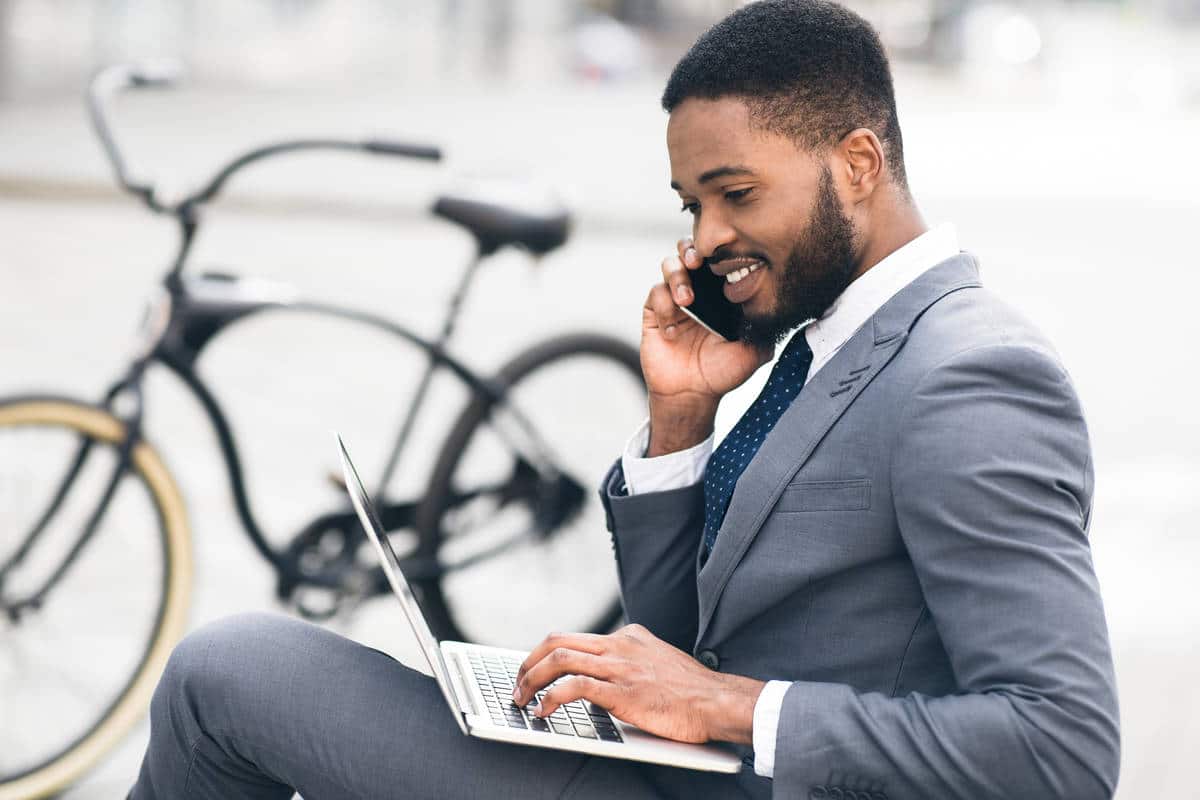 Happy entrepreneur working on laptop and talking on phone outdoors