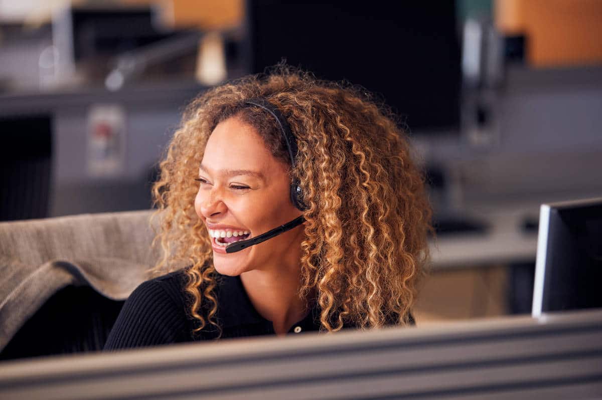 Laughing Businesswoman Wearing Telephone Headset Talking To Caller In Customer Services Department