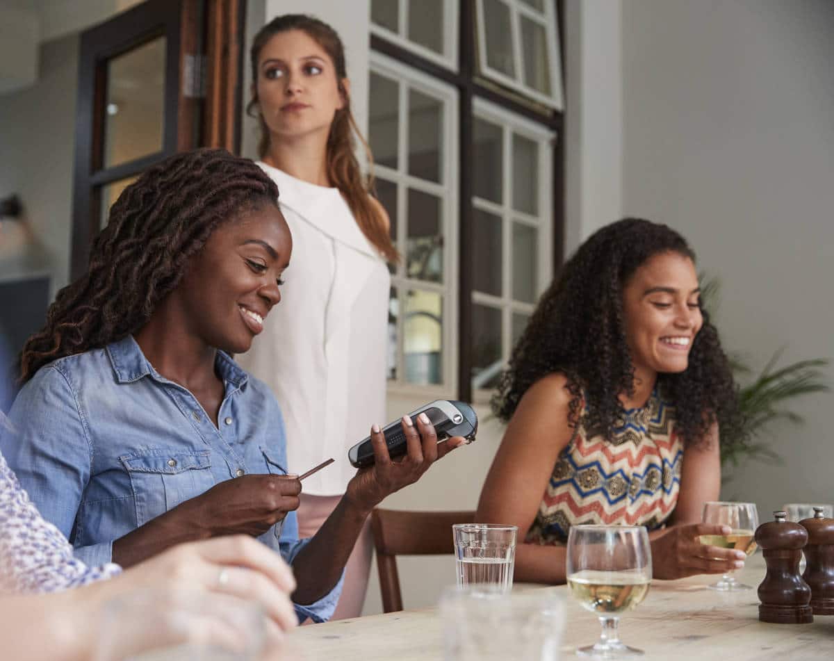 Female Customer In Restaurant Paying Bill Using Contactless Credit Card Terminal