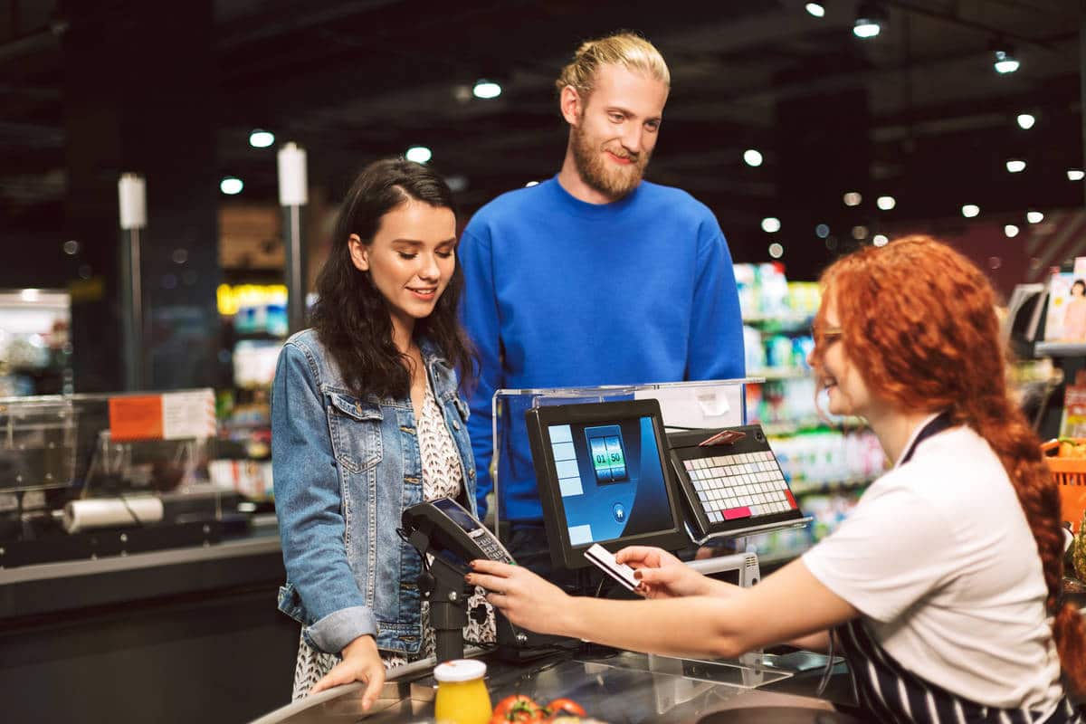 Young smiling couple standing near cashier desk happily paying 